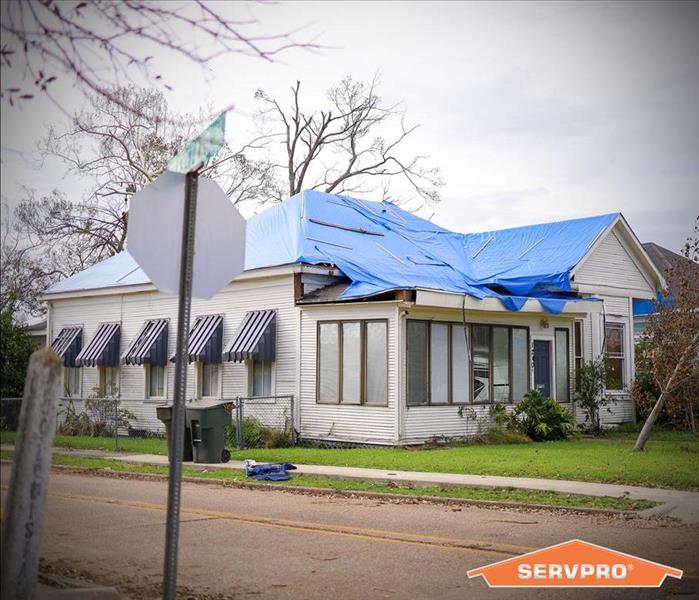 a home with a blue tarp secured to the damaged roof.